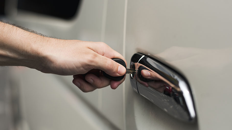 A close-up of a hand using a key fob to unlock a car door, highlighting the chrome handle and sleek vehicle design.