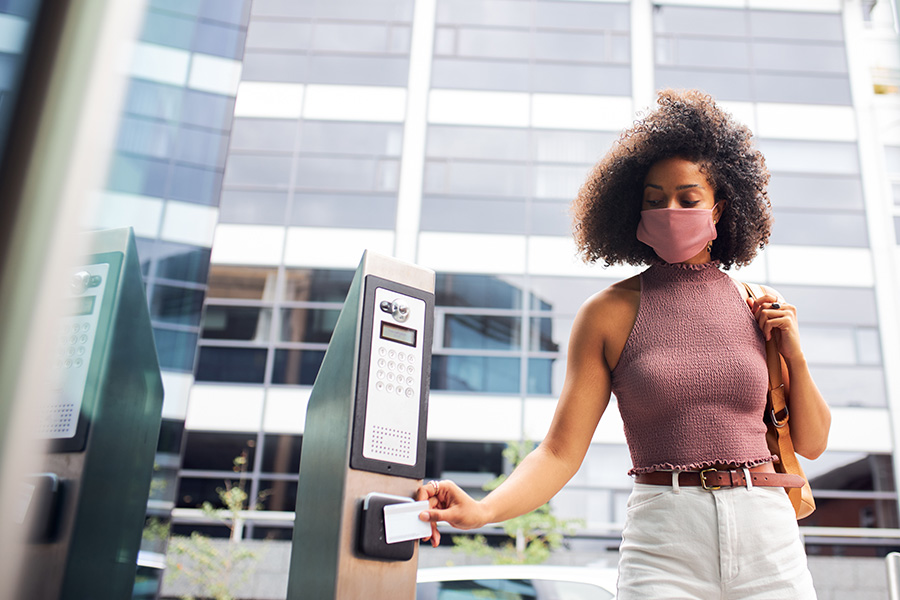 A woman in a sleeveless top uses a card reader at a parking kiosk in front of a modern building.
